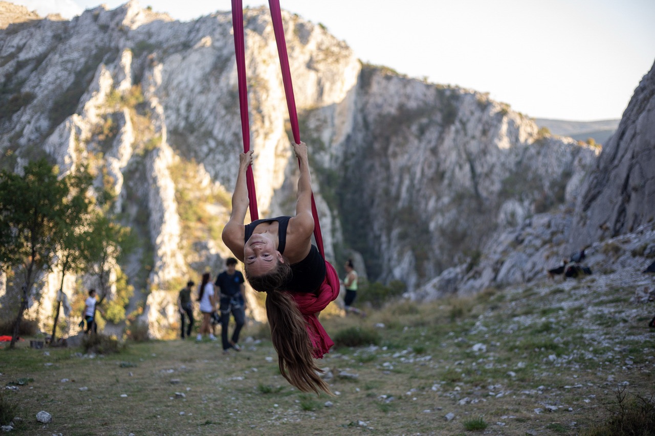 woman hanging upside down on red aerial silk in outdoor rocky mountainous area