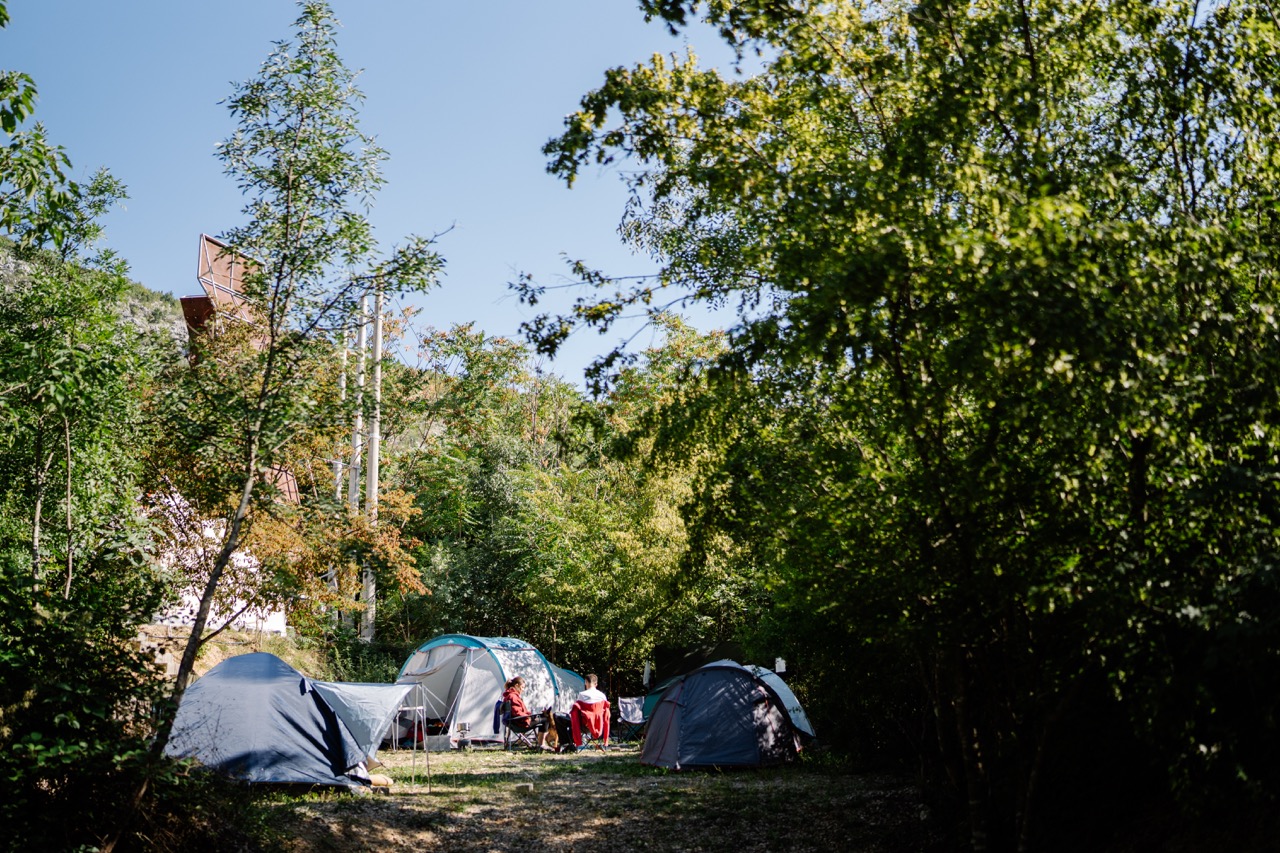 tents set up in a wooded campsite with two people sitting and chatting